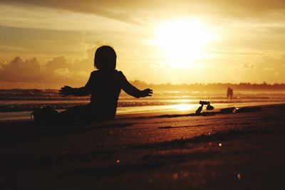 Silhouette girl sitting at beach during sunset