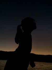 Silhouette woman standing at beach against sky during sunset