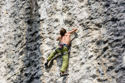 Rear view of shirtless man climbing on rock