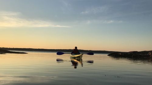 Man in sea against sky during sunset