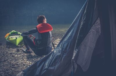 Rear view of man sitting by tent