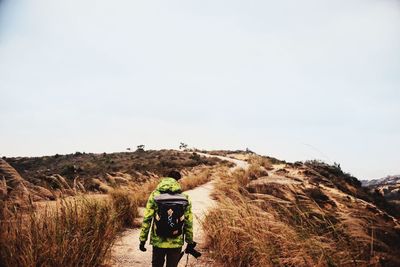 Rear view of man with backpack walking on trail at hill against sky
