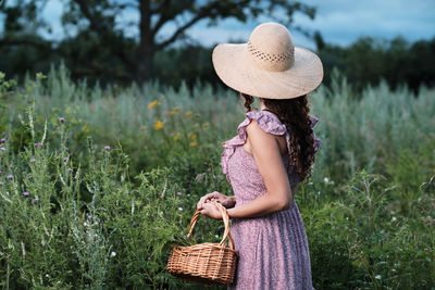Side view of young woman wearing hat standing against plants