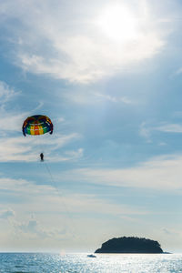 Mid distance view of person parasailing over sea against cloudy sky