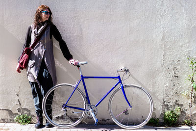 Young woman leaning on a city wall with vintage bike in sunny day