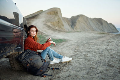 Young woman sitting on rock against mountains