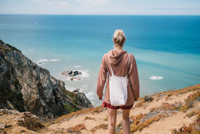 Rear view of man standing on rock by sea against sky