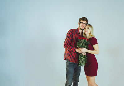 Portrait of young couple holding roses while standing against white background
