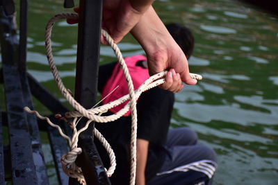 Cropped hands of person tying rope on metal