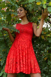 Beautiful young woman standing by plants against trees