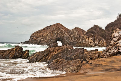 Rocks on beach by sea against sky