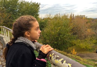 Side view of thoughtful girl standing by railing against sky