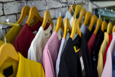 Cotton and sports t-shirts hung on wall hanger racks inside a clothes shop low-angle view.