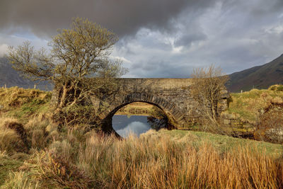 Arch bridge on field against sky