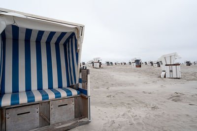 Hooded beach chairs on sand against clear sky