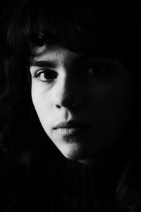 Close-up portrait of young woman against black background