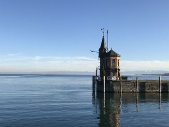 Traditional windmill on sea by building against sky