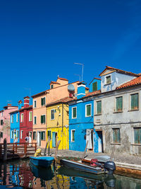 Boats moored on canal by buildings against blue sky