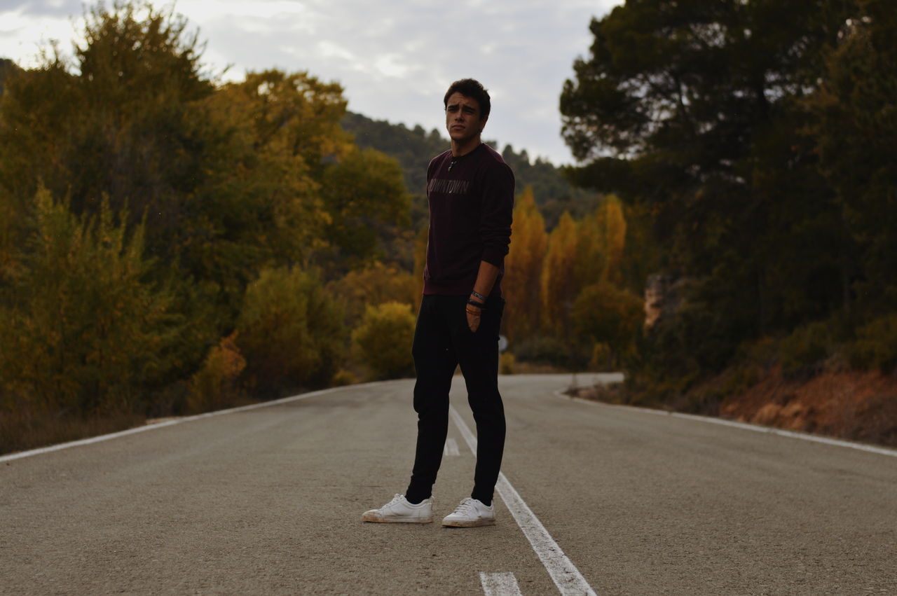 one person, real people, road, full length, tree, young adult, transportation, young men, lifestyles, standing, looking at camera, leisure activity, portrait, plant, casual clothing, nature, direction, day, men, outdoors