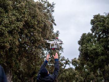 Rear view of man flying quadcopter against sky