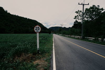 Road sign by trees against sky