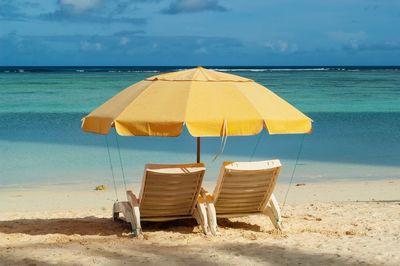 Deck chairs on beach by sea against sky