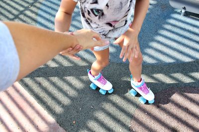 Cropped hand of mother assisting daughter roller skating on road