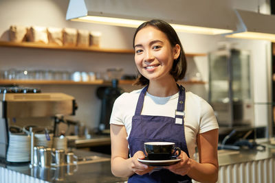 Young woman using mobile phone while standing in cafe