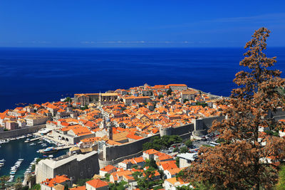 High angle view of cityscape by sea against clear blue sky