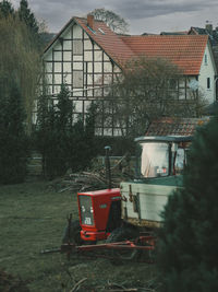 Red house on field by building against sky