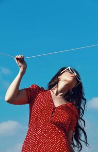 Young woman with arms raised standing against clear blue sky