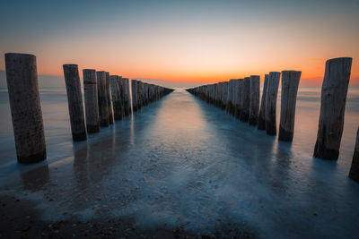 Wooden posts on beach against sky during sunset