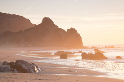 Rocks on beach against sky during sunset