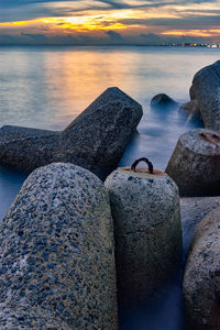 Rocks by sea against sky during sunset