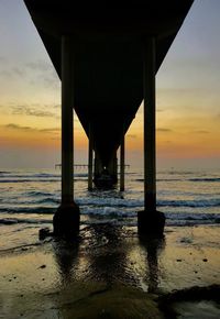Silhouette bridge over sea against sky during sunset
