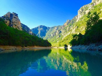 Scenic view of lake and mountains against clear blue sky