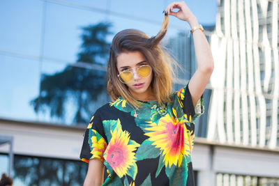 Portrait of young woman wearing sunglasses against building