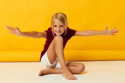 Portrait of smiling girl gesturing while sitting against yellow background
