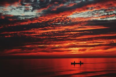 Silhouette boat in sea against dramatic sky during sunset