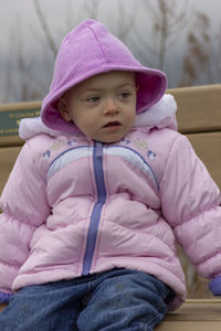 Cute baby girl wearing warm clothing sitting on bench