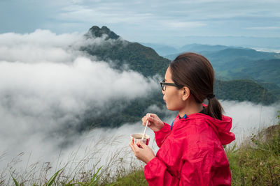 Young woman holding smart phone against mountains