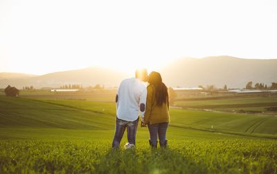 Rear view of couple kissing while standing on field against sky during sunset