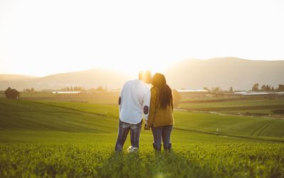 Rear view of friends standing on field against sky during sunset