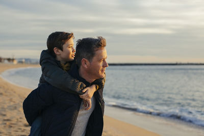 Father carrying son piggyback on the beach