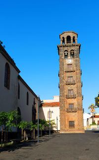 Bell tower of church in city against clear blue sky on sunny day