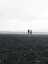 Silhouette couple walking on beach against sky