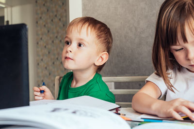 Boy sits at the table and looks at the laptop. focused children study at home remotely. 