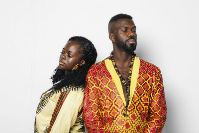 Trendy couple in stylish african clothes leaning to each other on white background with eyes closed