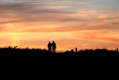 Silhouette men on field against sky during sunset