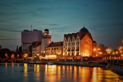 Illuminated buildings by river at dusk